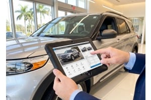 Car salesperson using a rugged Windows tablet to view vehicle details beside an SUV in a modern car dealership showroom