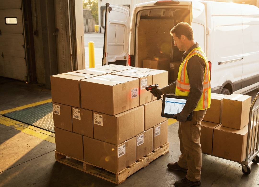 Warehouse worker scans pallet while holding rugged Windows tablet with inventory screen at loading dock